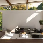 Bright and airy living room with large windows, neutral tones, and natural light streaming in, highlighting minimalistic furniture and greenery outside.