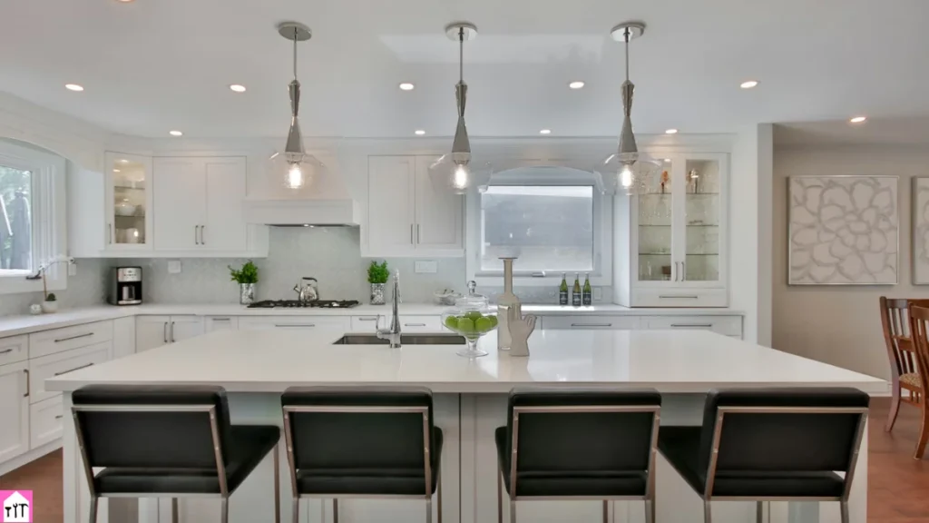 Modern white kitchen interior with Luxury Kitchen Cabinets, large island, pendant lighting, and sleek black bar stools.