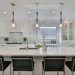 Modern white kitchen interior with Luxury Kitchen Cabinets, large island, pendant lighting, and sleek black bar stools.
